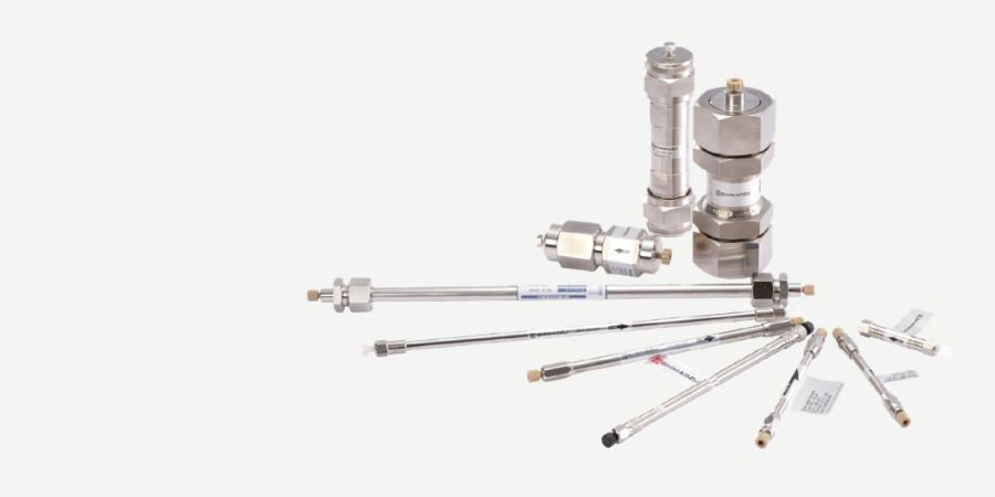 Collection of stainless-steel HPLC columns, guard columns and flow components arranged on a white background.